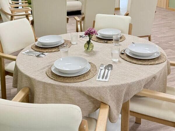 Mesa redonda decorada con platos, cubiertos y un pequeño ramo de flores. Sillas alrededor.