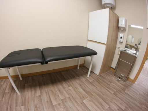 Camilla de tratamiento en una sala con pared beige y armario blanco. Suelo de madera.