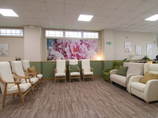Sala de espera con sillas blancas, sofá, y decoración floral en la pared.