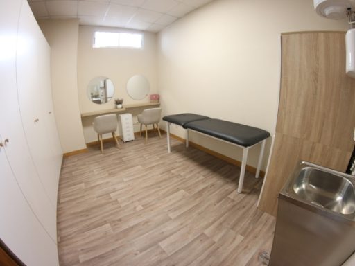 Sala de tratamiento con camilla, lavabo y dos sillas frente a un espejo.