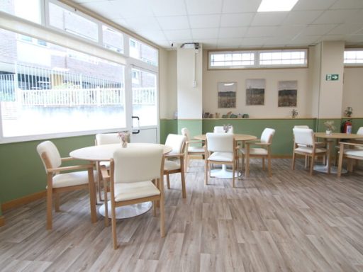 Interior de una cafetería con mesas y sillas blancas sobre un suelo de madera.