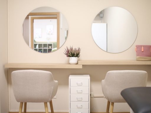 Dos espejos redondos sobre un tocador minimalista con sillas y una planta.