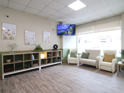 Sala de espera luminosa con sillones, estantería y televisión en la pared.