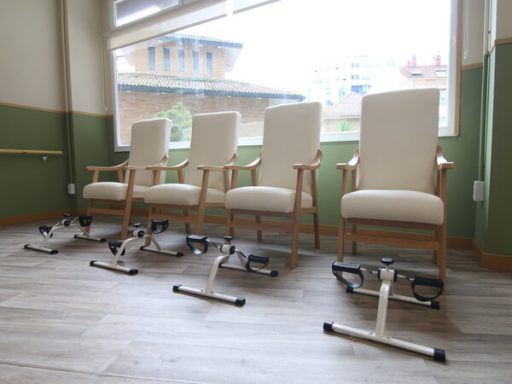 Cuatro sillas de ruedas blancas alineadas junto a una ventana en un ambiente luminoso.